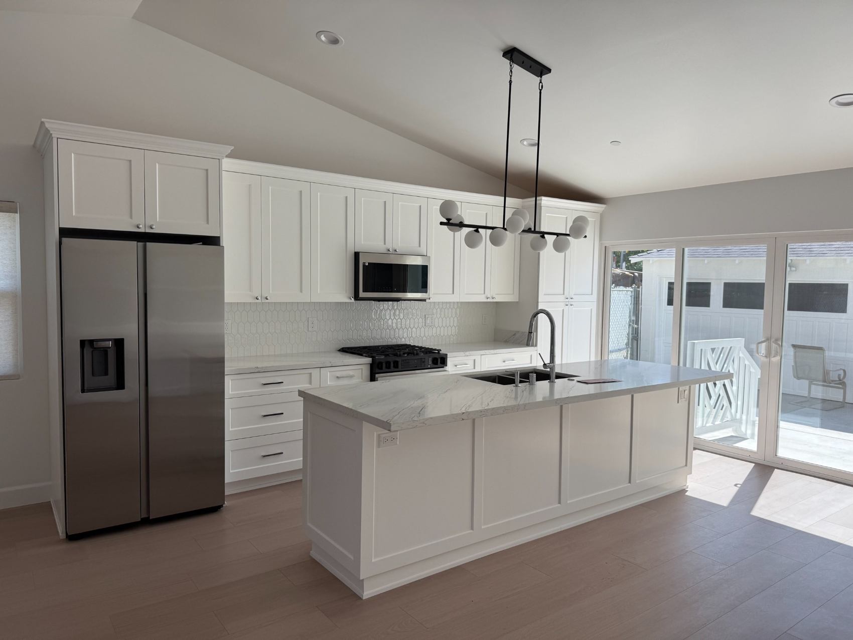 Completed kitchen renovation with white cabinetry, a large marble-look island and pendant lighting